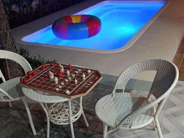 Two chairs and a Thai checkers table beside the floodlit pool at night